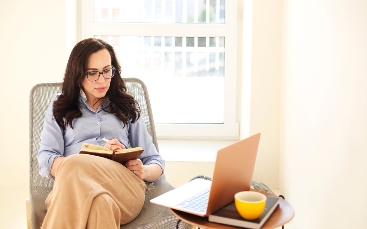 Adult businesswoman with laptop writing in notepad