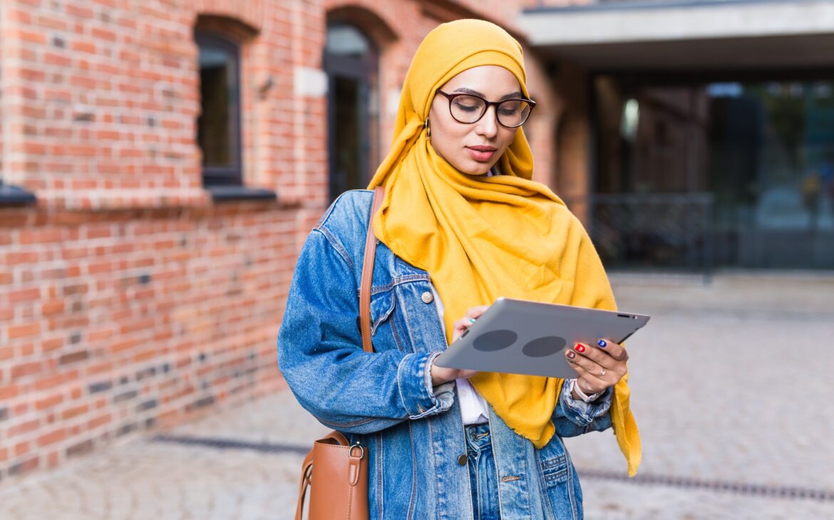 Arab woman student. Beautiful muslim female student wearing bright yellow hijab holding tablet