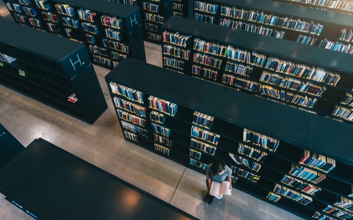 Female student at library bookshelf reading book