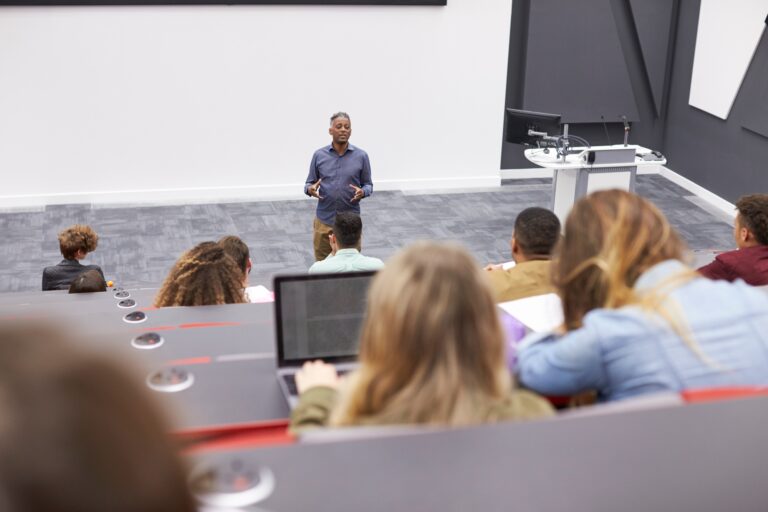 Man lectures students in lecture theatre, back row seat POV