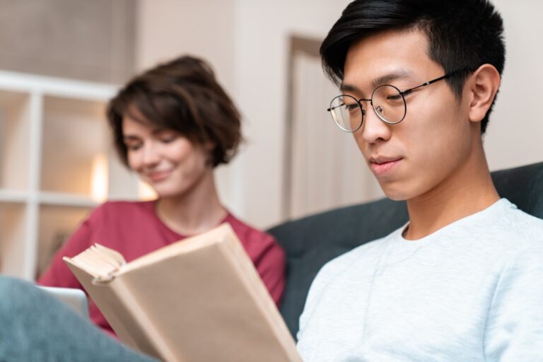 Photo of pleased multinational couple reading book and using laptop