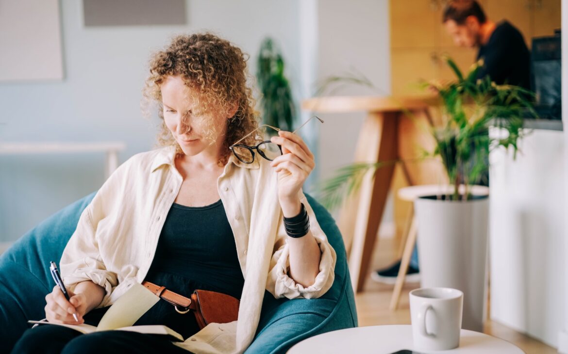 Woman puts on glasses and writes in paper notebook